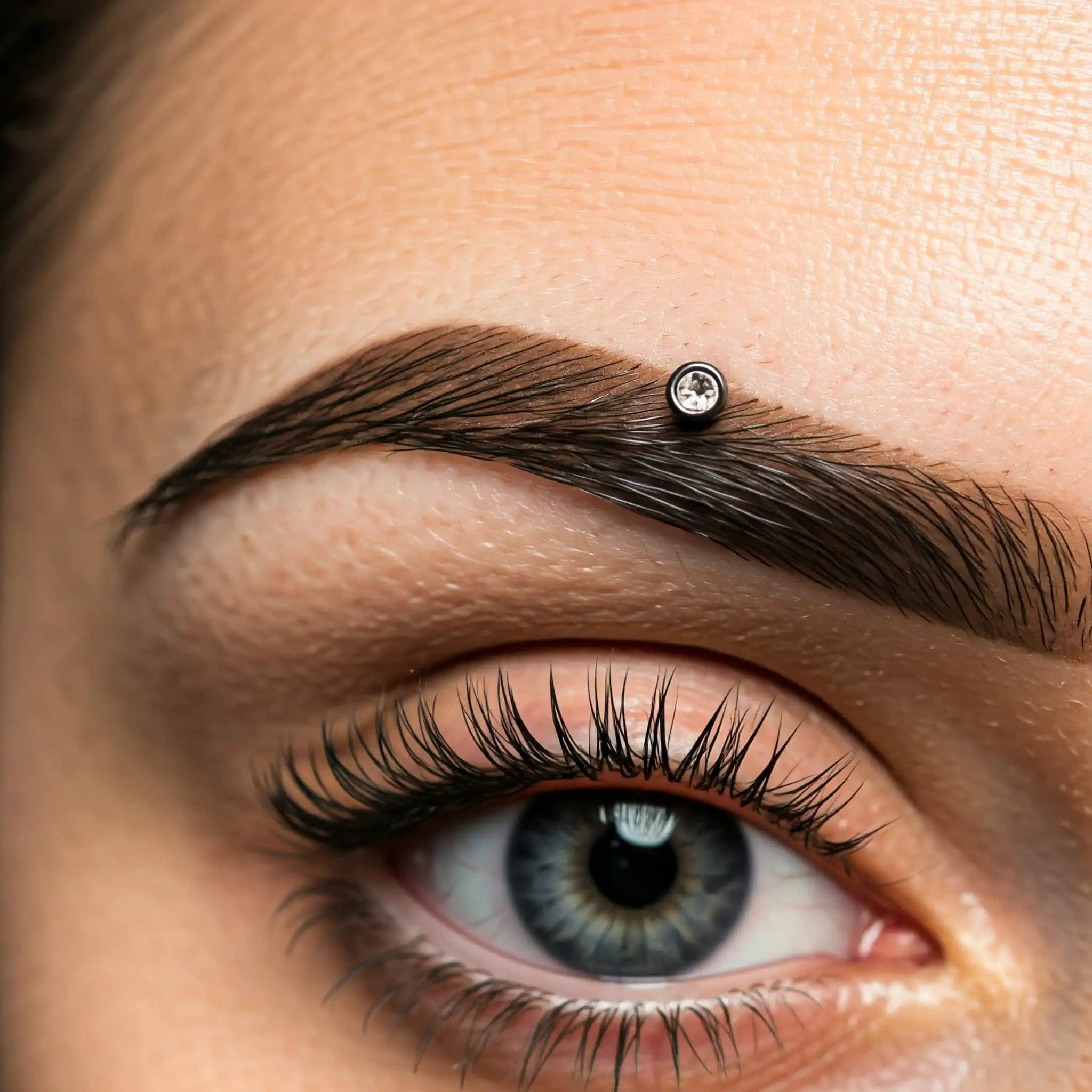 Image of a dermal eyebrow piercing with a decorative stud, emphasizing contemporary piercing trends.