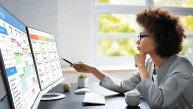 A professional woman in business attire analyzing schedules and tasks on dual monitors displaying a calendar, planner, and time tracking software.